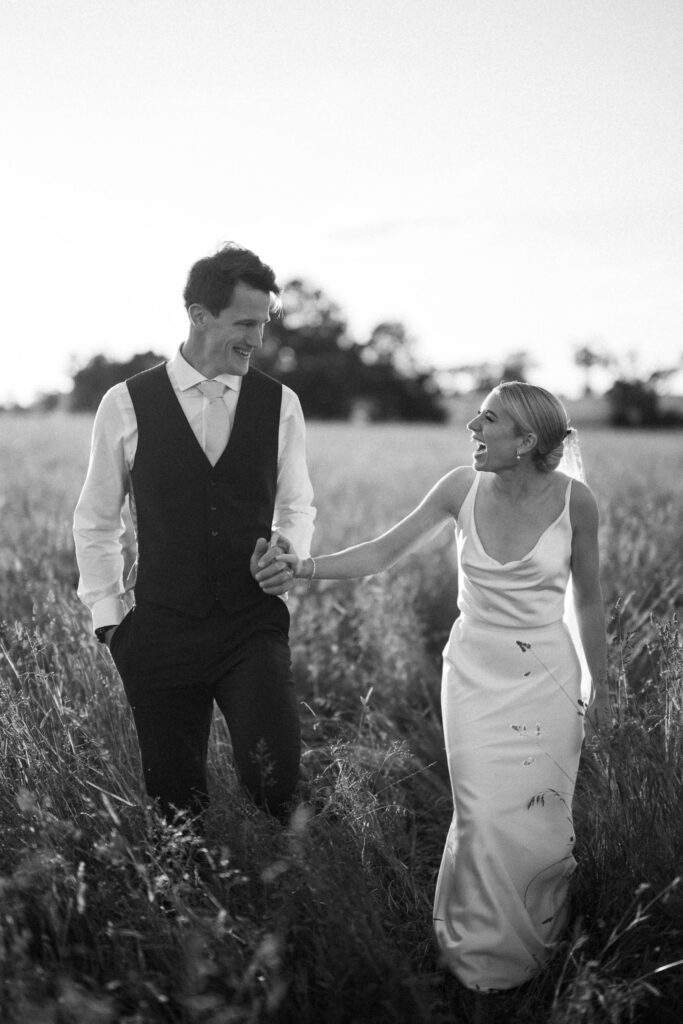 Bride and groom walking through long grass during golden hour
