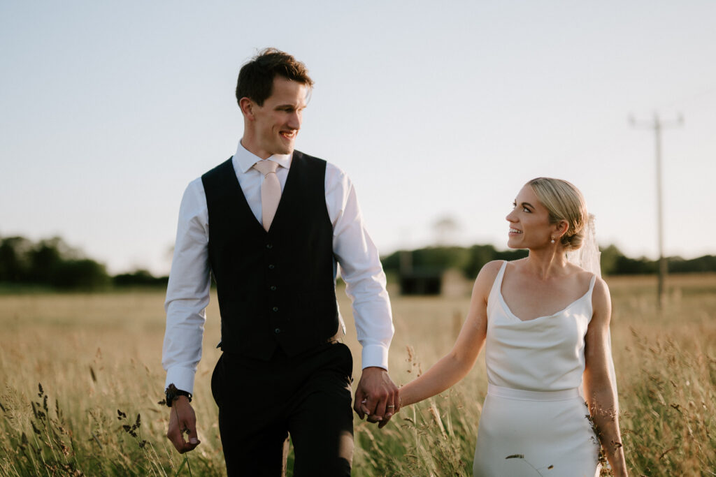 Bride and groom holding hands during golden hour portraits in a field