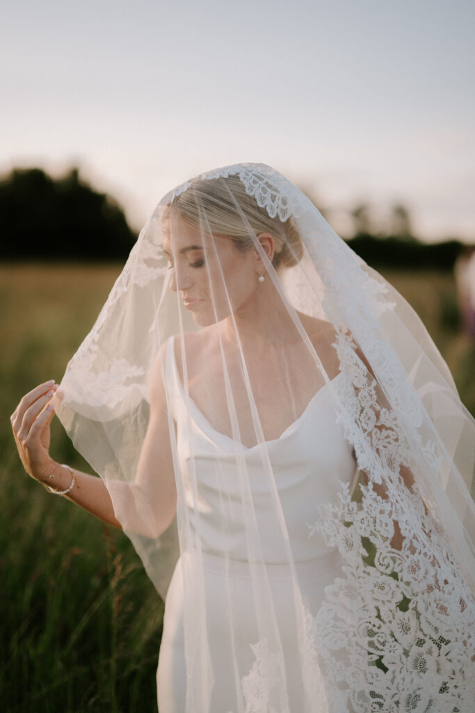 Bride wearing lace veil during golden hour portraits in a Suffolk field