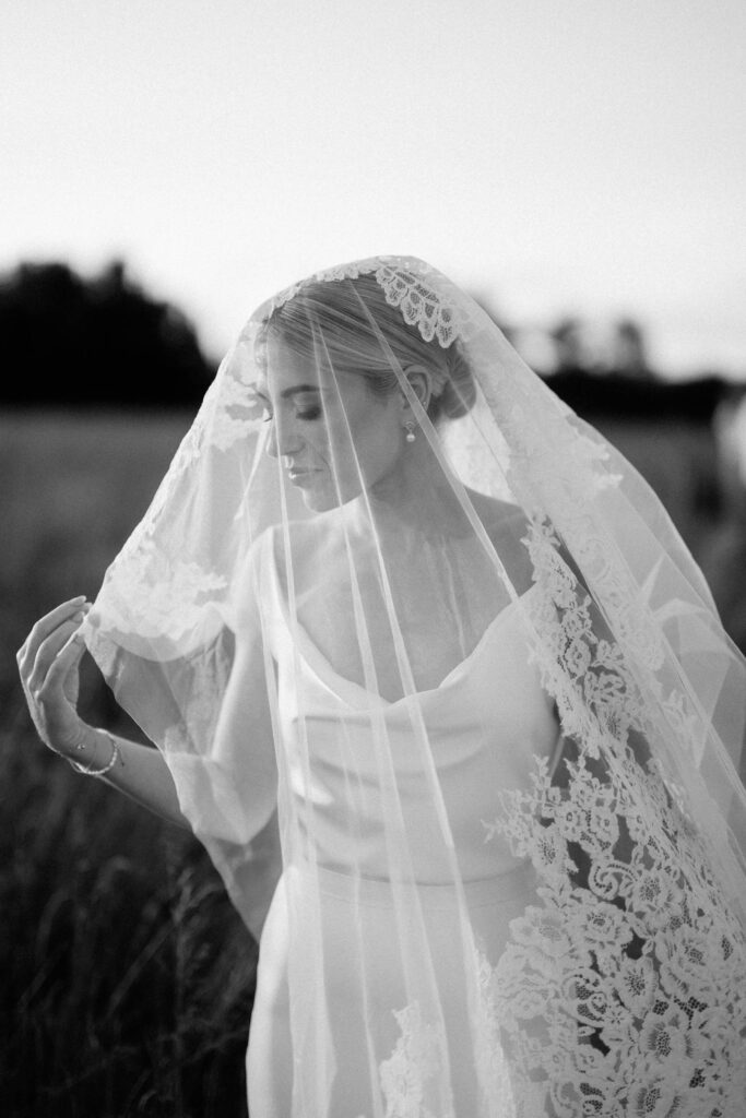 Bride wearing lace veil during golden hour portraits in a Suffolk field