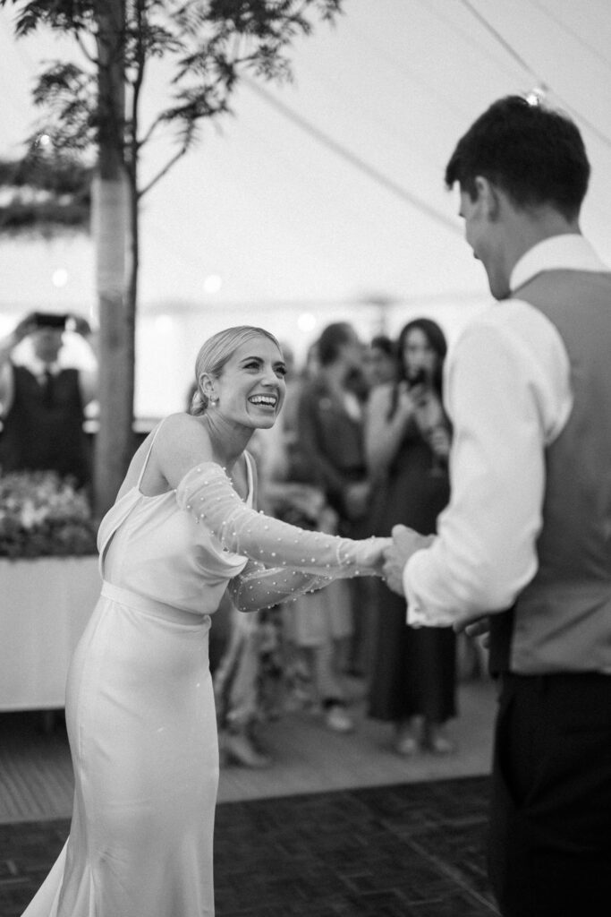 Bride reaching for groom during first dance at marquee wedding reception