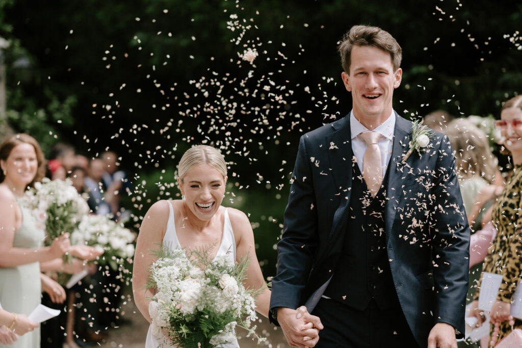 Bride and groom holding hands during confetti exit outside the church