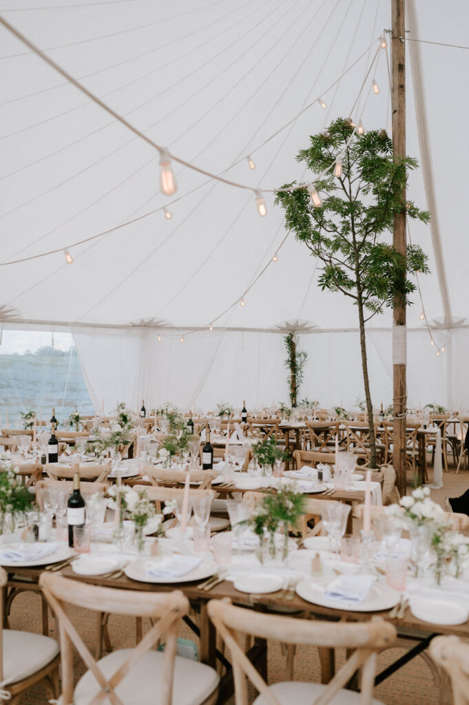 Marquee wedding reception set up with long tables and greenery and festoon lights