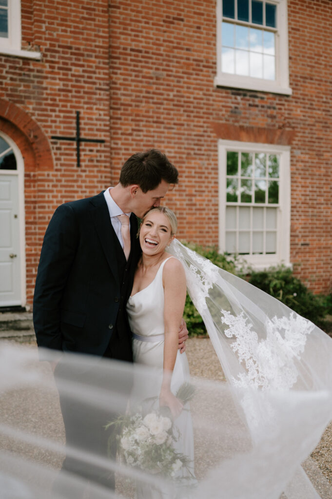 Bride and groom standing close together with the veil blowing in the breeze
