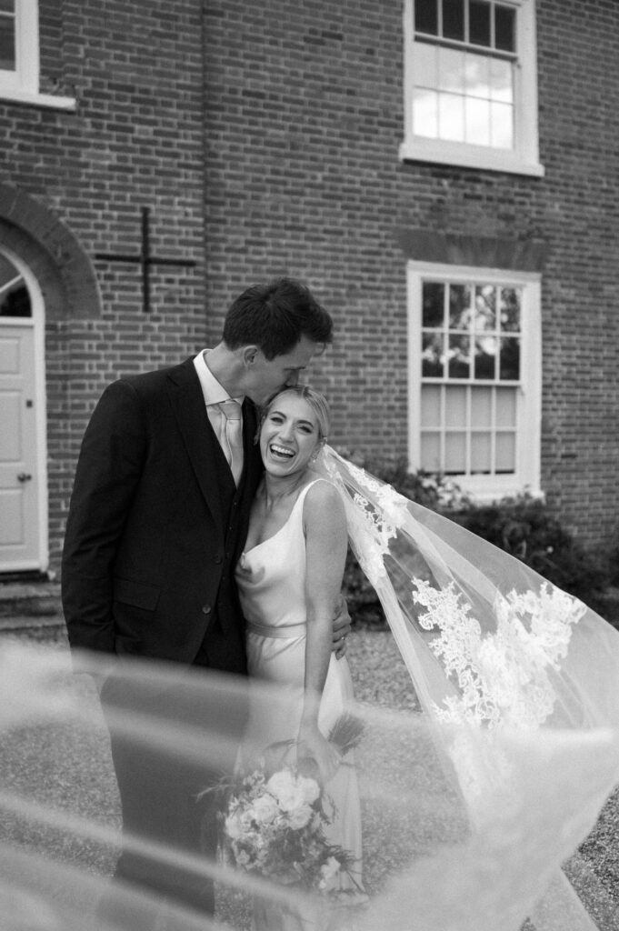 Bride and groom standing close together with the veil blowing in the breeze
