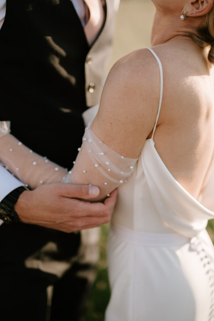 Close up of bride’s wedding dress sleeve with pearl beaded detail during golden hour portraits
